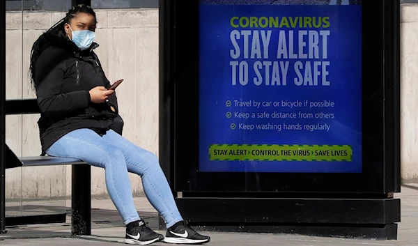 A woman waits at a bus stop showing the new government slogan in London, Tuesday, May 12, 2020, as the country continues in lockdown. (AP)