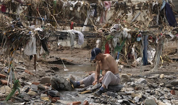 A man washes his clothes in a stream near debris left over after flood waters devastated the village of Nanxinfang on the outskirts of Beijing, on August 4, 2023. (AP)