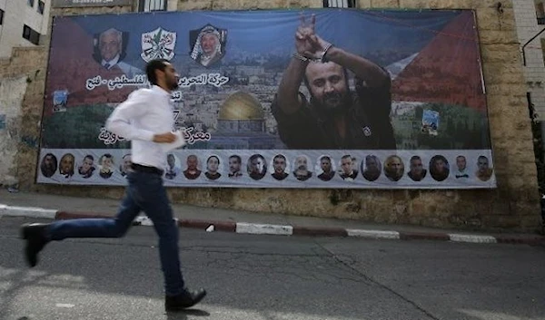 A Palestinian runs past a poster bearing a portrait of the Dean of Palestinian prisoners, Marwan al-Barghouti, in the West Bank city of Ramallah, Occupied Palestine, on May 3, 2017. (AFP/Abbas Momani)