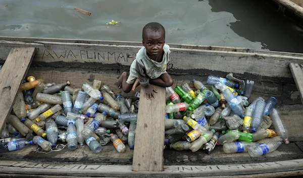 A child sits inside a canoe with empty plastic bottles he collected to sell for recycling in the floating slum of Makoko in Lagos, Nigeria, Nov. 8, 2022. (AP)