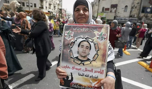 A woman carries a poster bearing the image of a Palestinian prisoner in Israeli prison during a demonstration marking Palestinian Prisoners' Day in Ramallah on 17 April 2022. (AFP)