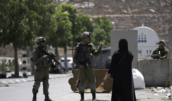 IOF soldiers speak to a Palestinian woman near the site of an attack near a colonial settlement in Al-Khalil, Aug. 30, 2023. (AP)