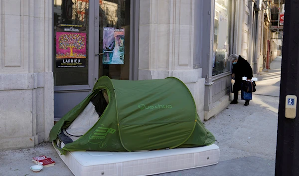 A woman stands in a street next to a homeless tent, in Paris, France, Tuesday, Dec. 21, 2021 (AP)