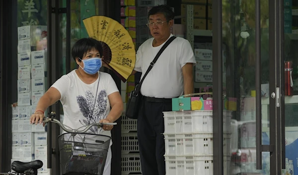 A woman pushes a bicycle past a man cooling himself with a fan at a store on a hot day in Beijing, July 24, 2023. (AP)