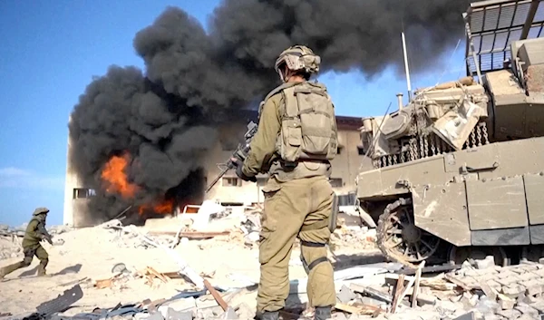 Israeli invading soldier holds a weapon as smoke billows from explosion in the background, in Gaza City, Nov. 14, 2023 (AP)