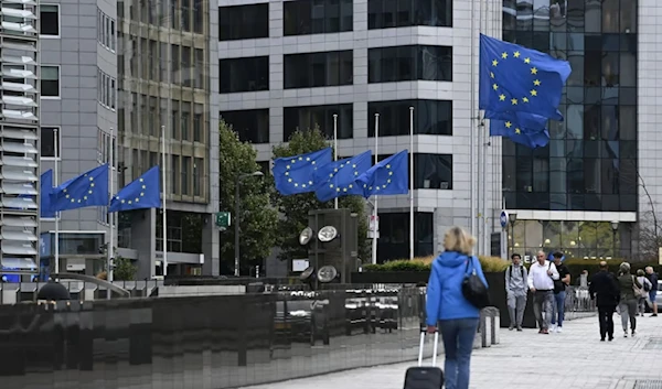 Pedestrians walk past as European Union flags flap, in front of European Union headquarters in Brussels, Thursday, Dec. 28, 2023. (AFP)