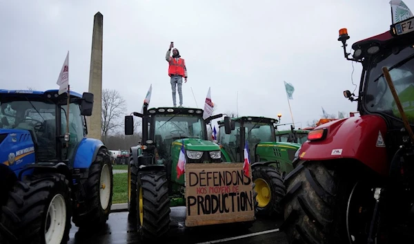 A farmer stands atop a tractor as farmers block a roundabout in Fontainebleau, south of Paris, Friday, Jan. 26, 2024 (AP)