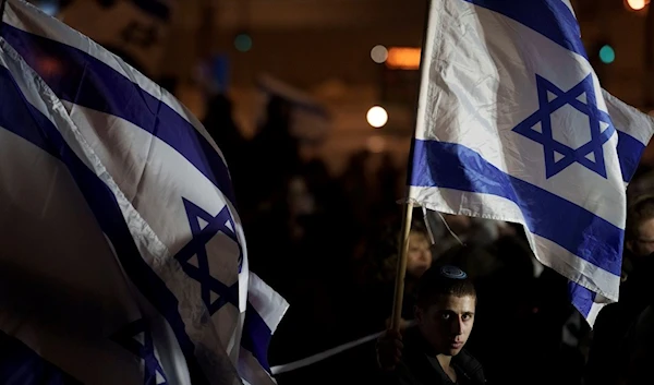 People wave Israeli flags during a protest against humanitarian aid entering Gaza and against the hostages exchange deal with Hamas, in Jerusalem, Israel, Thursday, Jan. 25, 2024 (AP)