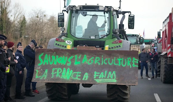 Police forces watch a farmerdriving his tractor with inscription "Save farming, France is hungry" on a highway, Monday, Jan. 29, 2024 in Argenteuil, north of Paris. (AP)