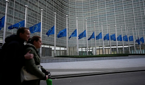 Two people ride on a scooter as EU flags flap in the wind at half staff, in remembrance of former European Commission President Jacques Delors, in front of EU headquarters in Brussels, Dec. 28, 2023.