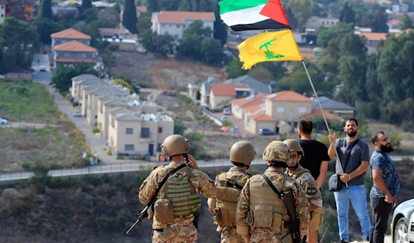 Lebanese soldiers stand on a hill that overlooks the Israeli settlement of "Metulla", background, as a man waves the Palestinian and Hezbollah flags in Lebanon, Monday, Oct. 9, 2023 (AP)