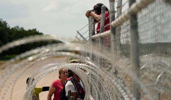 Migrants who crossed the Rio Grande from Mexico into the U.S. climb a fence with barbed wire and concertina wire, Monday, Aug. 21, 2023, in Eagle Pass, Texas. (AP Photo/Eric Gay)