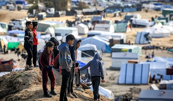 Forcibly displaced Palestinian children stand atop a small hill near tents at a make-shift shelter for Palestinians in Rafah in the southern Gaza Strip on January 30, 2024 amid the ongoing Israeli genocide. (AFP)