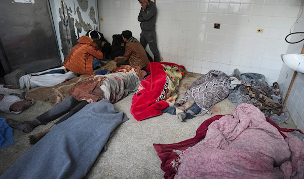 Palestinians kneel next to the bodies of relatives killed in the Israeli bombardment of the Gaza Strip, inside a morgue of Al Aqsa hospital, in Deir al Balah, Gaza Strip, Monday, Feb. 12, 2024. (AP)