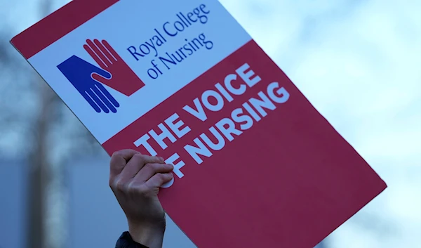 A demonstrator holds up a placard in support of the strike by nurses outside St Thoma's Hospital in London, Tuesday, Dec. 20, 2022(AP)