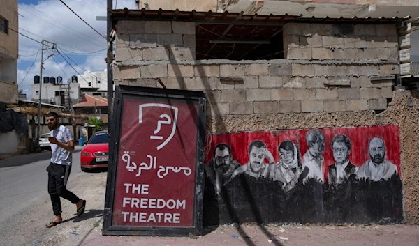 A Palestinian man walks past graffiti that depicts late notable Palestinians, at the entrance of the Freedom Theatre, April 12, 2022 (AP)