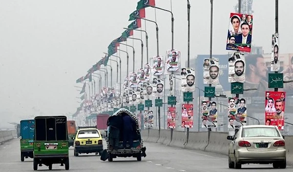 Commuters move past the election posters installed on light poles along a road in Peshawar ahead of the upcoming general elections. (AFP)