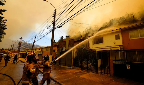 Firefighters protectively spray water on homes as forest fires burn nearby, in Vina del Mar, Chile, Saturday, Feb. 3, 2024. (AP)