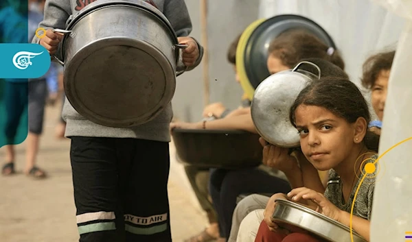 Children in Gaza sit holding pots and pans, hoping to get some food for their families. (Al Mayadeen Net)