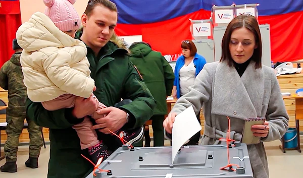 Photo by the Russian Defense Ministry Press Service on March 15, 2024, a Russian serviceman is with his child as his wife casts her ballot at a polling station during the presidential election at an undisclosed location in Russia. (AP)