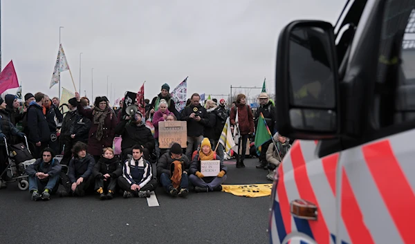 Climate activists sit on the ground, in front of a police van, blocking the main highway around Amsterdam near the former headquarters of an ING bank to protest its financing of fossil fuels, Saturday, Dec. 30, 2023.(AP)