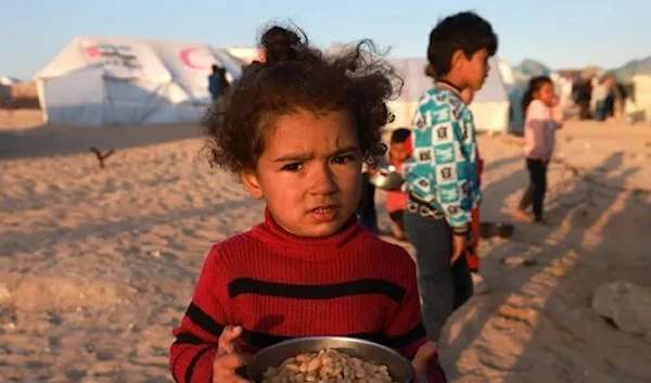 A Palestinian girl holds a bowl of beans before an iftar meal in Rafah in the southern Gaza Strip amid the Israeli genocidal war (AFP)