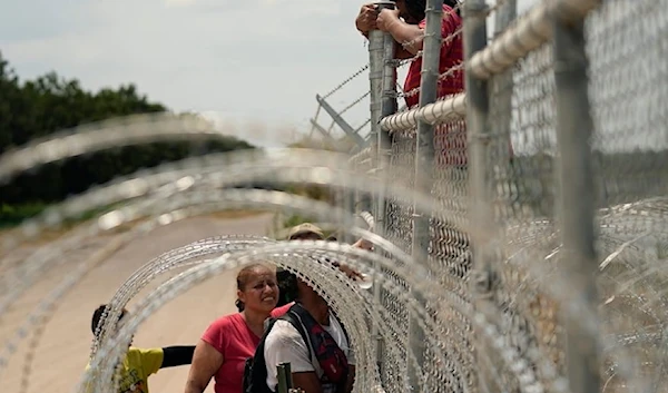 Migrants who crossed the Rio Grande from Mexico into the US climb a fence barbed wire and concertina wire, Monday August 21,2023, in Texas. (AP)