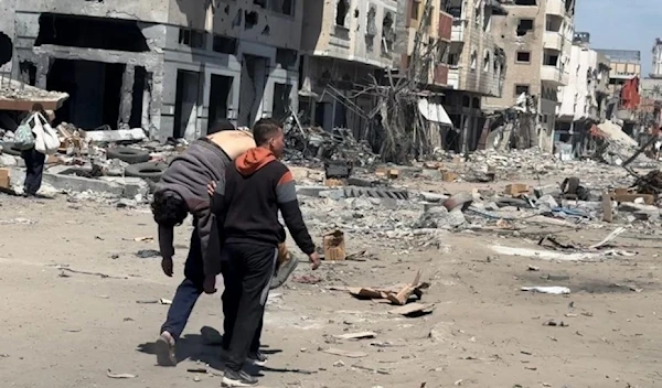 A Palestinian man carrying the body of his son who was martyred when 'Israel' opened fire on people waiting for aid (Social Media)