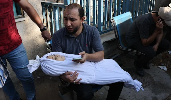 A Palestinian father holds his little son wrapped in a shroud during a funeral for victims killed in a building that was hit by an Israeli air strike on October 12, 2023. (AFP)