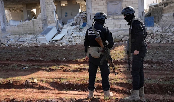 Militants of the terrorist organization Hayat Tahrir al-Sham stand in front of a destroyed house in Atareb, Syria, Sunday, Feb. 12, 2023. (AP)