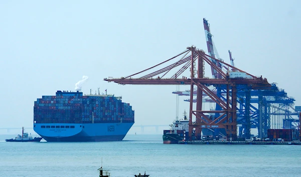 A man on a boat fishes as a container vessel prepares to dock at a port in Xiamen in southeast China's Fujian province on Dec. 27, 2023.(AP)