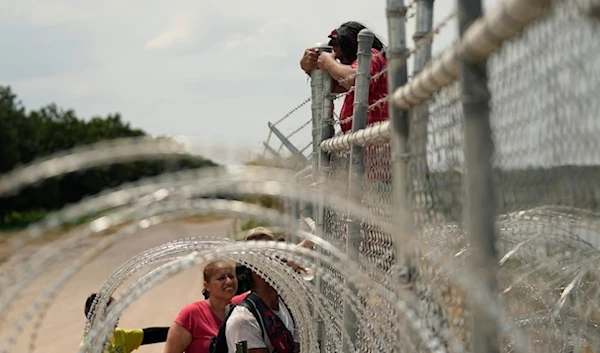 Migrants who crossed the Rio Grande from Mexico into the US climb a fence with barbed wire and concertina wire in 2023, in Eagle Pass, Texas. (AP)