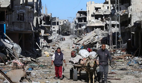 Palestinians walk through the rubble resulting from the Israeli occupation forces' bombardment of Khan Younis, Gaza Strip, Friday, March 8, 2024. (AP)