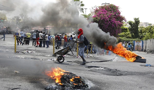 A man pushes a wheelbarrow past burning tires during a protest demanding the resignation of Prime Minister Ariel Henry, in Port-au-Prince, Haiti, Thursday, March 7, 2024.