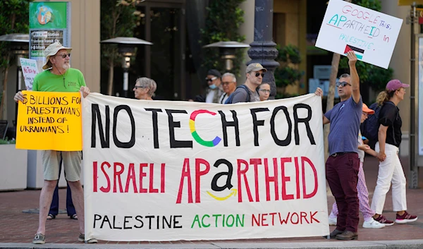 Two men hold up a banner and signs along Market Street during a tech workers protest against Google and Amazon for their contracts with the Israeli occupation government in San Francisco, Thursday, Sept. 8, 2022.(AP)