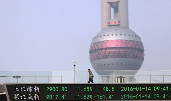 A pedestrian walks across an elevated bridge showing index figures for the Shanghai, top, and Shenzhen, bottom, stock exchanges in Shanghai, January 14, 2016. (AP)