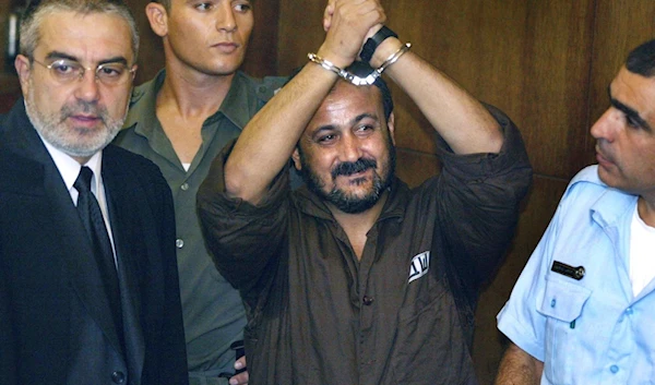 Marwan Barghouti, center, raises his handcuffed hands in the air on the opening day of his trial in 'Tel Aviv', occupied Palestine on Aug. 14, 2002.(AP)