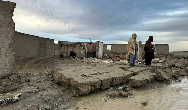 People stand over the wall of their damaged house caused by flooding due to heavy rains in the area near Chaman, Pakistan, Thursday, April 18 2024 (AP)