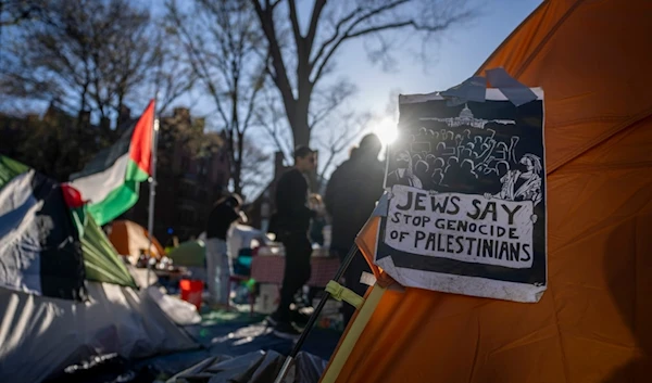 Students protesting against the war on Gaza stand next to a Palestinian flag and tents at an encampment in Harvard Yard, at Harvard University in Cambridge, Mass., on Thursday, April 25, 2024 (AP Photo/Ben Curtis)