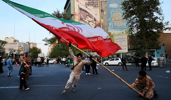 Demonstrators wave a huge Iranian flag in their anti-Israeli gathering in front of an anti-Israeli banner on the wall of a building at the Felestin Sq. in Tehran, Iran, Monday, April 15, 2024.