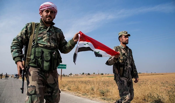 Syrian Arab Army forces carry a national flag as they walk at a checkpoint near the town of Tal Tamr, north Syria, on Oct. 22, 2019. (AP)