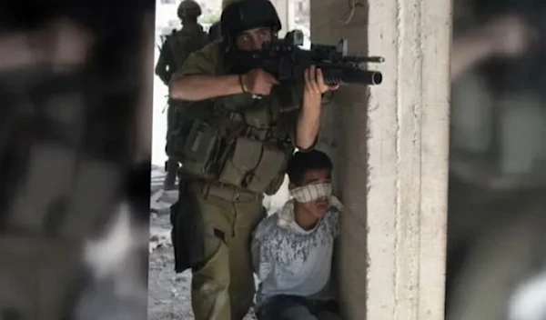 An undated image showing the Israeli occupation forces using a Palestinian child as a human shield. (Social media)