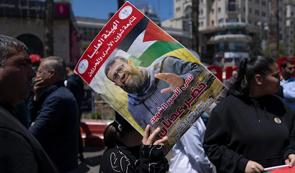 A Palestinian activist holding a poster with the name and picture of PIJ official Khader Adnan, who was martyred after a 86 days hunger strike, during a protest in the West Bank city of Ramallah, May 2, 2023 (AP)