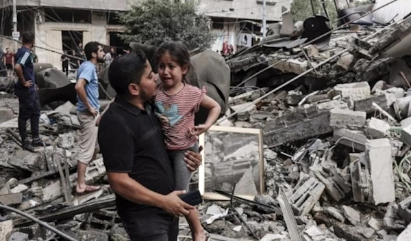 A Palestinian father carries his crying son as he walks in front of a building destroyed in an Israeli air strike in Gaza City on October 7, 2023. (AFP)