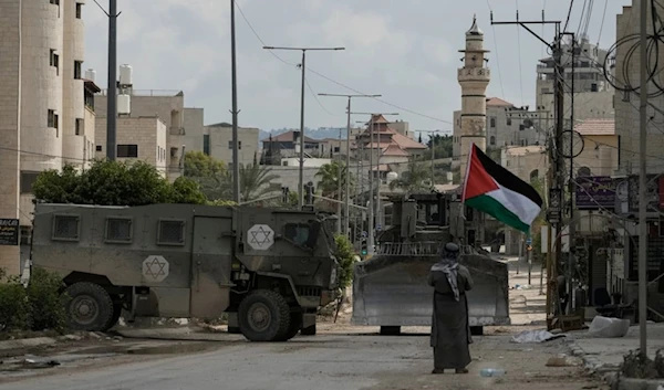 Renowned Palestinian activist Khairi Hanoon waves the Palestinian flag as a convoy of Israeli occupation military armored vechiles drives by during an aggression on Tulkarm, in the occupied West Bank, on September 3,2024. (AP)