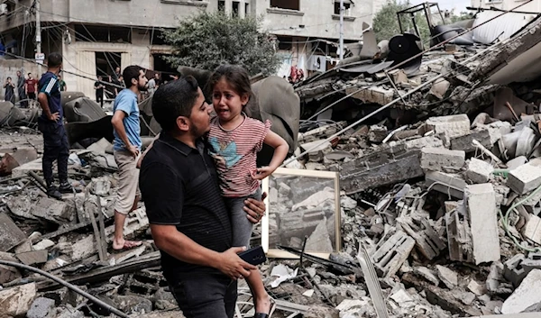 A Palestinian father carries his traumatized child as he walks in front of a residential building destroyed in an Israeli airstrike on Gaza City on October 7, 2023. (AFP)