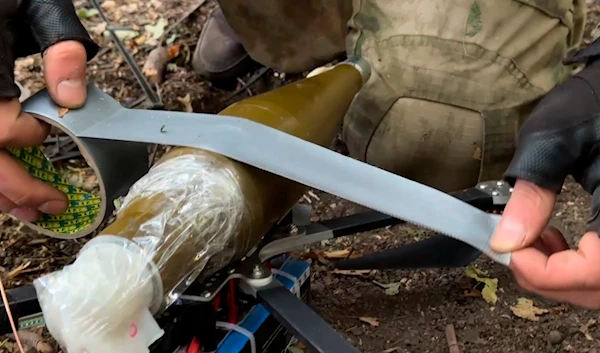 In this photo taken from a video released by Russian Defense Ministry press service on Sept. 26, 2024, A Russian serviceman attaches a grenade to a FPV-drone at a border area of Kursk region, Russia. (AP)