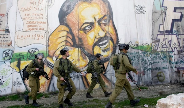 Israeli separation wall with portrait of leader Marwan Barghouti,with Israeli occupation soldiers patroling infront of it in the West Bank city of Ramallah, occupied Palestine, March 8, 2012. (AP)