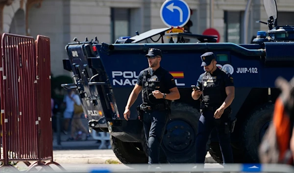 Police officers walk by a police armoured vehicle before the last stage of La Vuelta cycling race in Madrid, Spain, Sunday, Sept. 8, 2024. (AP Photo/Paul White)