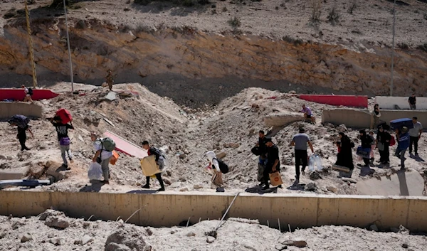 People carry their luggage as they cross into Syria on foot, through a crater caused by Israeli airstrikes aiming to block Beirut-Damascus highway at the Masnaa crossing, in the eastern Bekaa Valley, Lebanon, Saturday, Oct. 5, 2024. (AP)